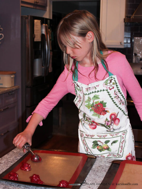 girl dropping cookie dough onto baking sheet